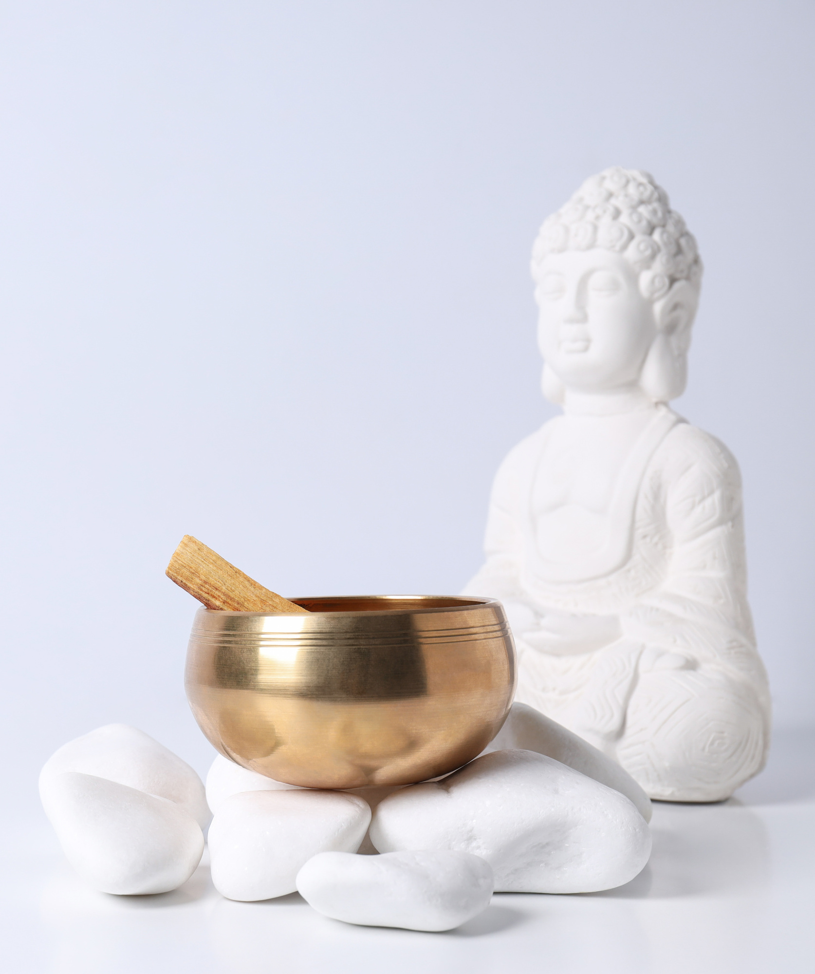Bowl on stones and Buddha statue on white background, space for text